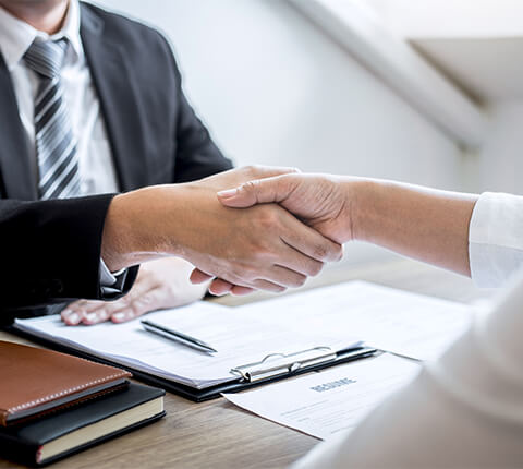 Man shaking a women's hand over a desk with pen and clipboard.