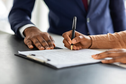 Woman signing a document with pen next to a man